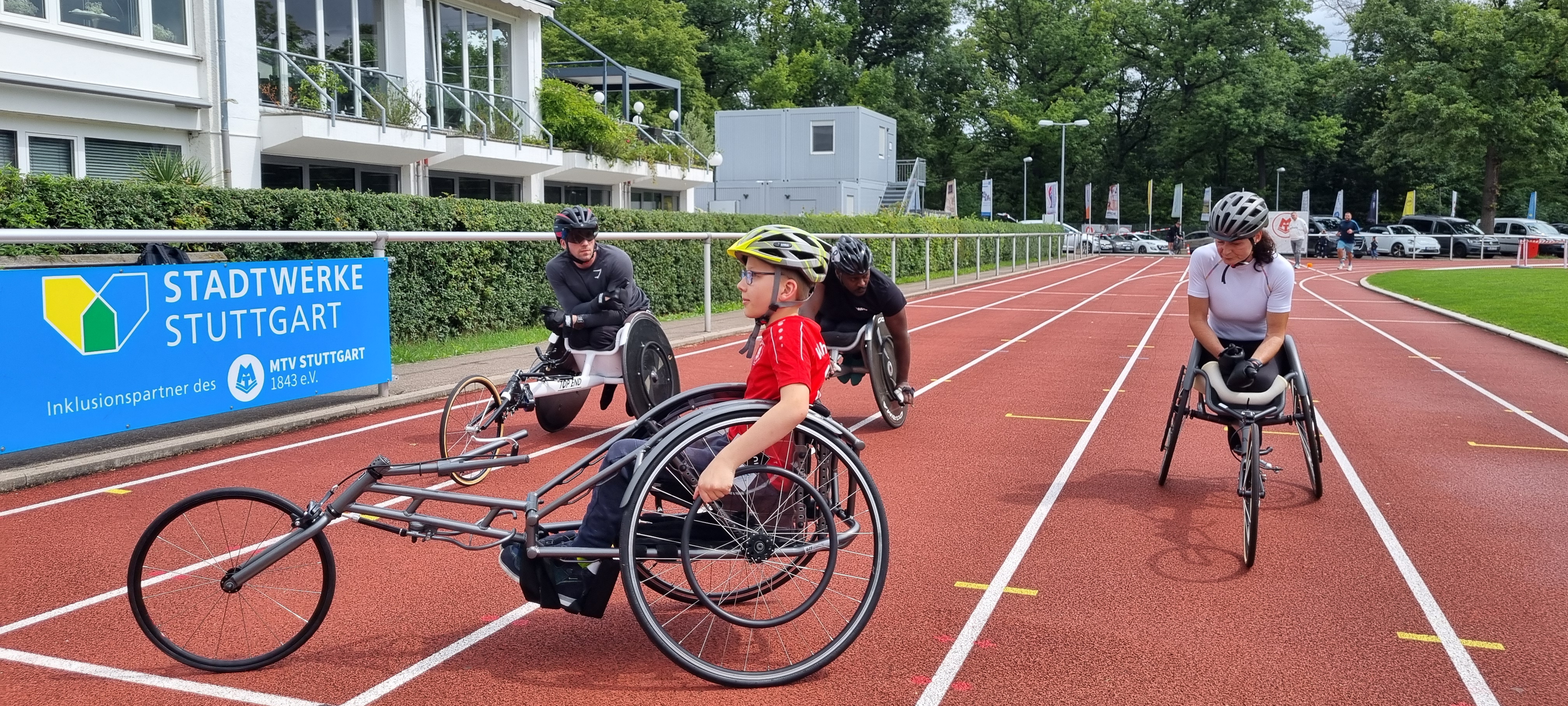 Drei Sportler im Rennrollstuhl auf der Tartanbahn.
