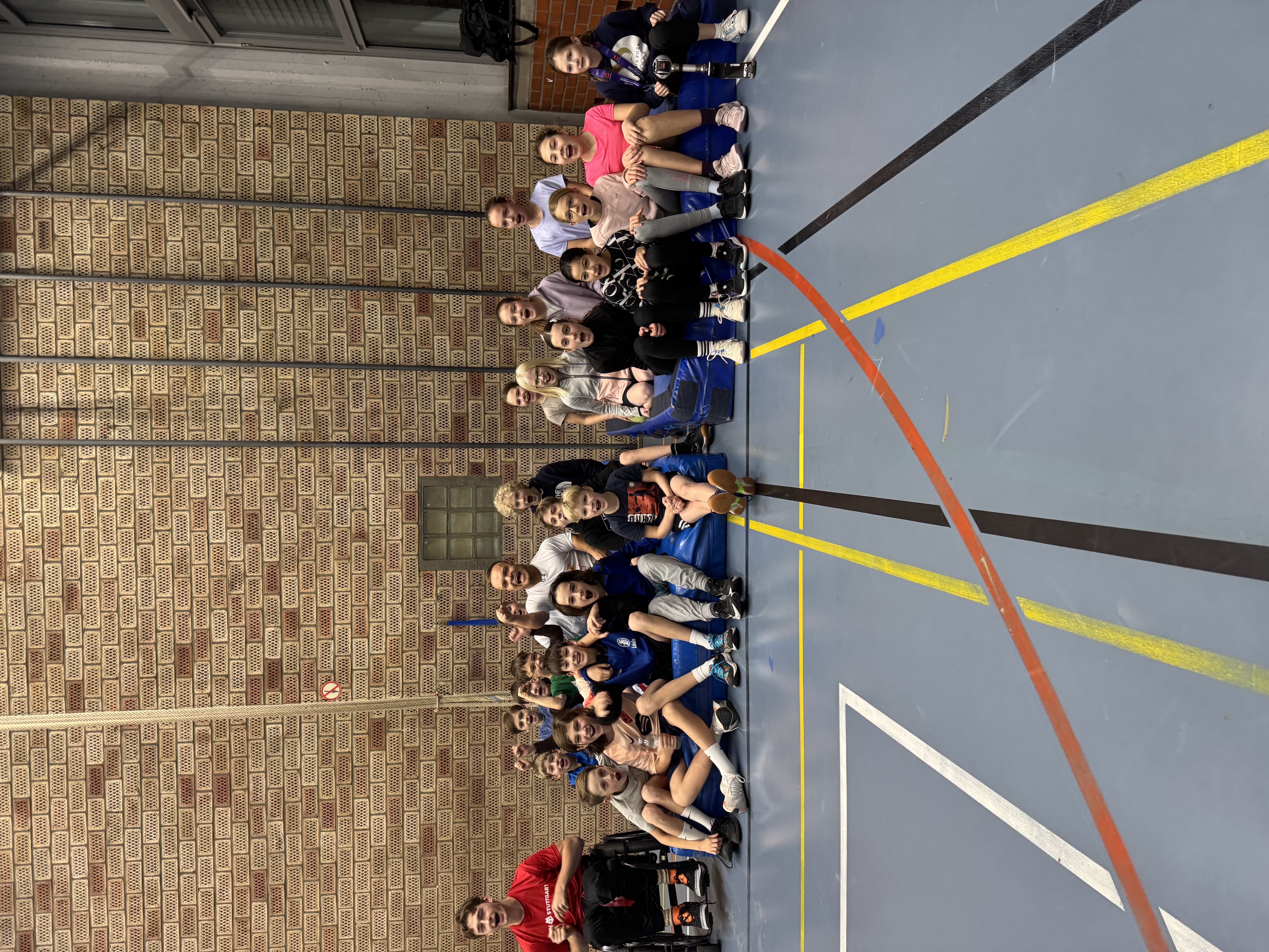 Eine Gruppe Kinder und Niko Kappel sitzen auf Weichbodenmatten, daneben steht ein jugendlicher Rollstuhlfahrer. Alle jubeln mit offenem Mund, teilweise sind Fäuste gestreckt.