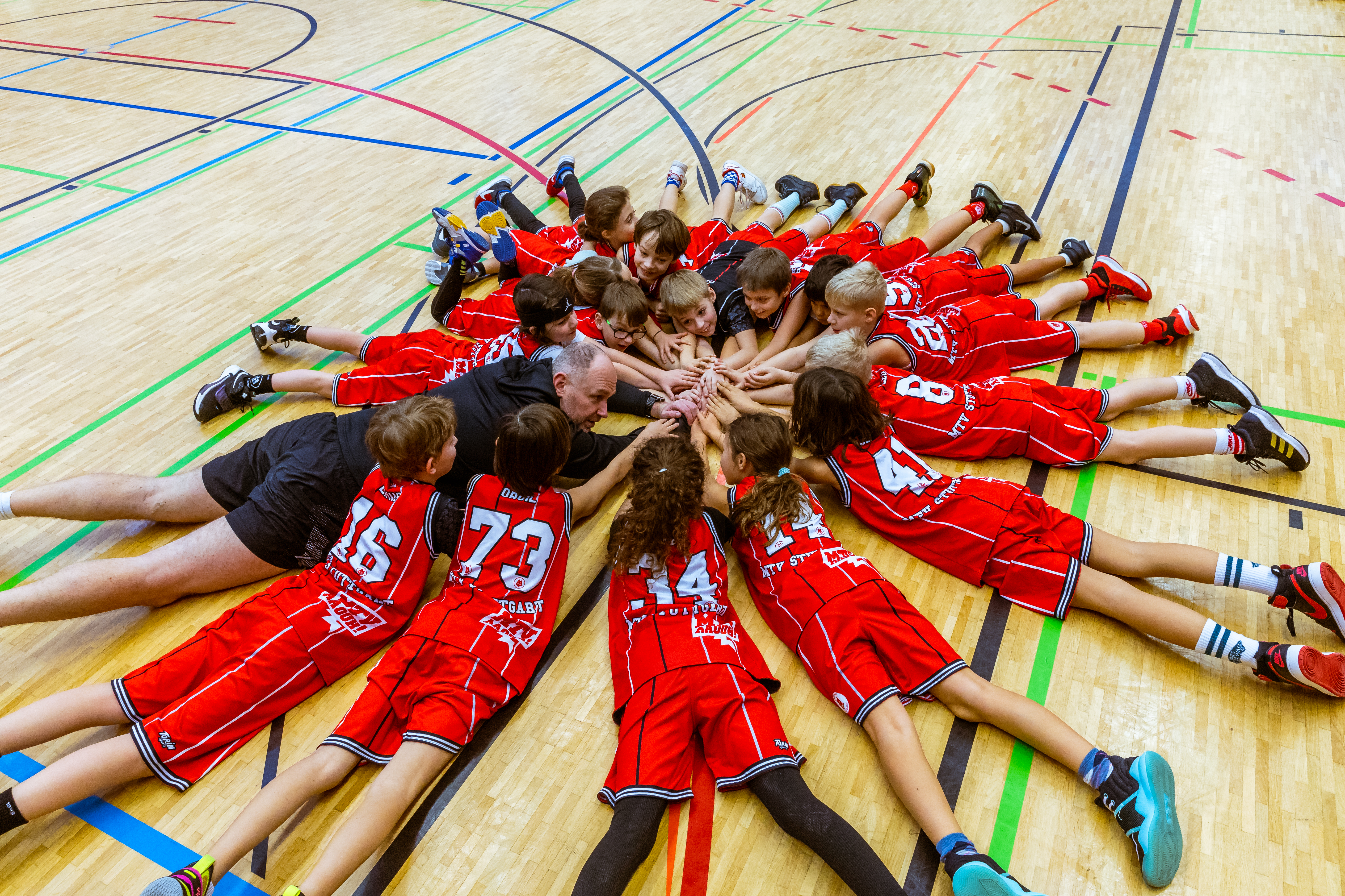 Auf diesem Foto sehen Sie alle Kinder zusammen mit Athletiktrainer Daniel Graf auf dem Boden