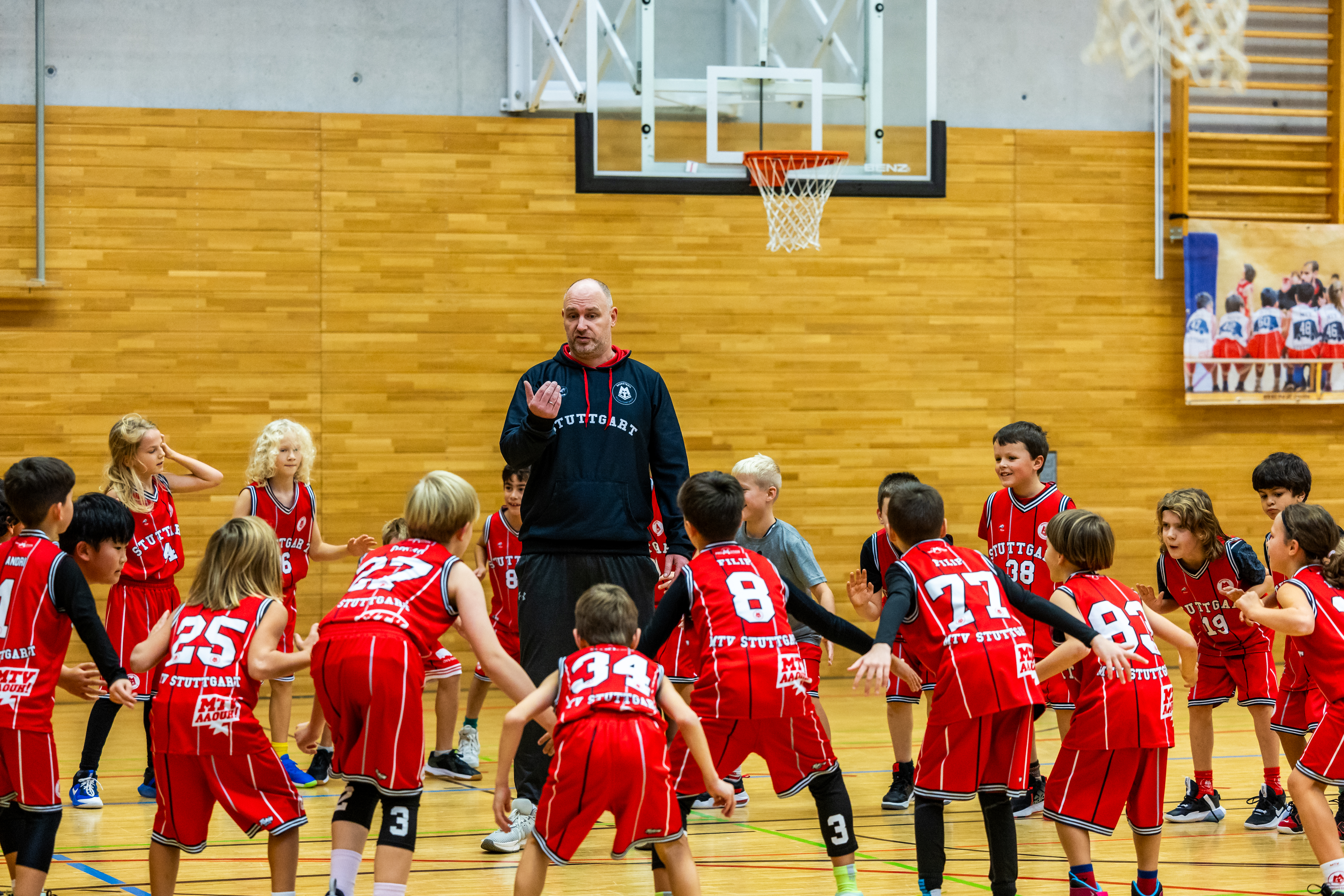 das Foto zeigt die Kinder mit dem Rücken zugewandt bei der Fußarbeit, während der Athletiktrainer erklärt