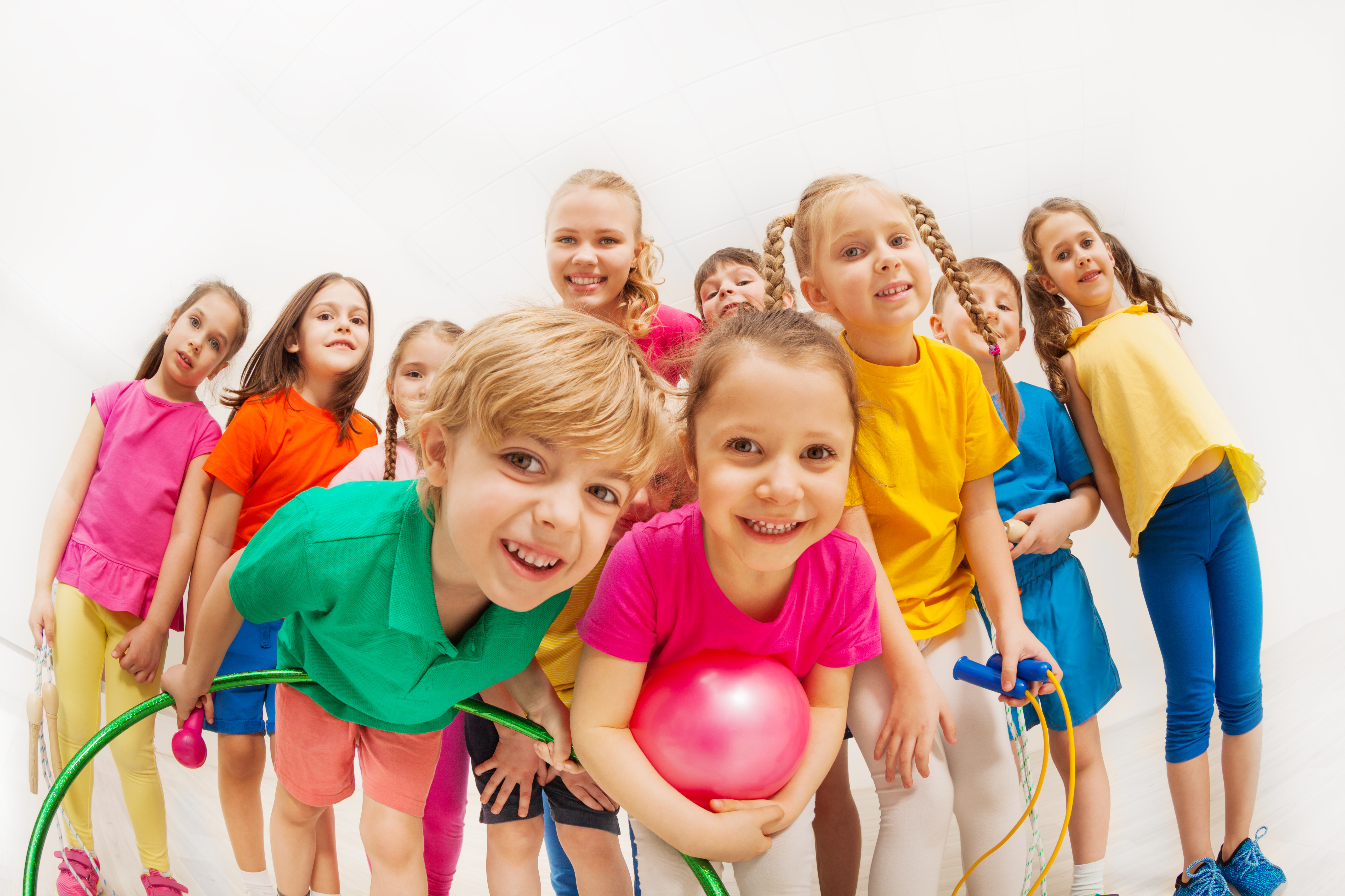 Das Bild zeigt 10 Kinder, die alle in die Kamera schauen. Viele von Ihnen haben Kleingeräte, wie z.B. Springseil, Gymnastikball oder Reifen in der Hand.