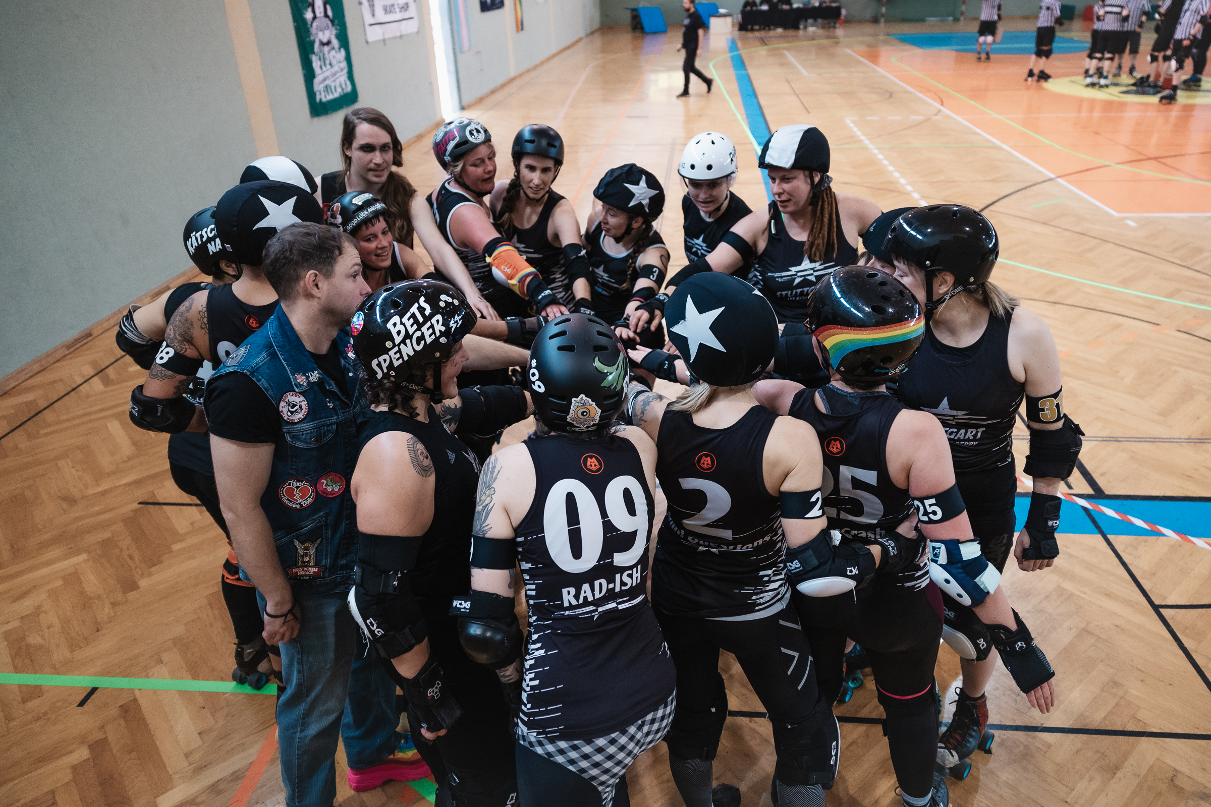 Das Bild zeigt ein Roller-Derby-Team bei ihrem Huddle. Die Spielerinnen stehen im Kreis zusammen und strecken die Hände in die Kreismitte zusammen.