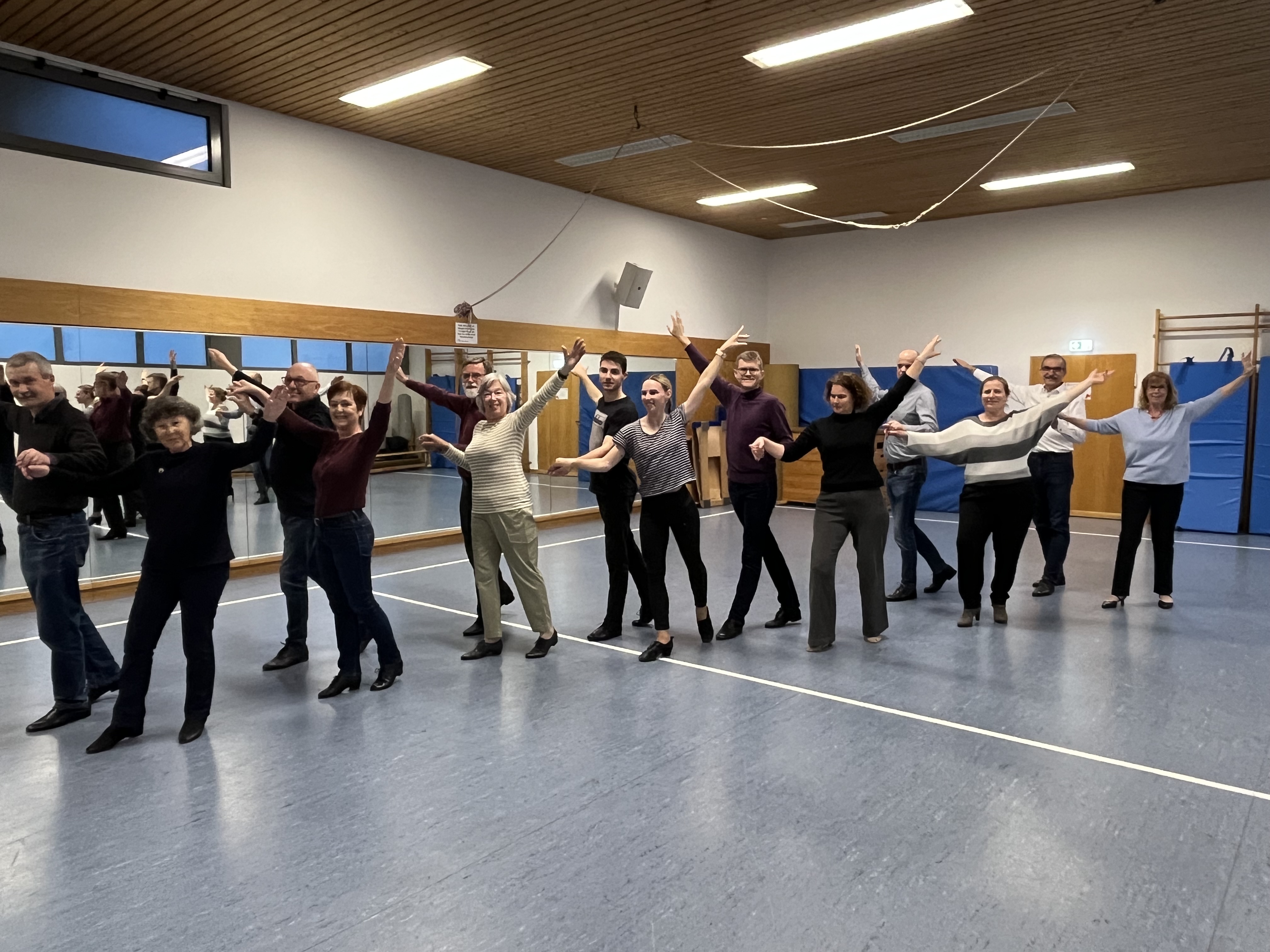 Das Bild zeigt 7 Tanzpaare diagonal in der großen Gymnastikhalle des MTV stehend, mit dem Körper und dem Gesicht - wie immer beim Tanzen - dem Betrachter zugewandt. , Die Damen jeweils links des Herren, die Hände der Paare sind gefasst, die freien Arme schräg nach oben in Tanzpose ausgestreckt.