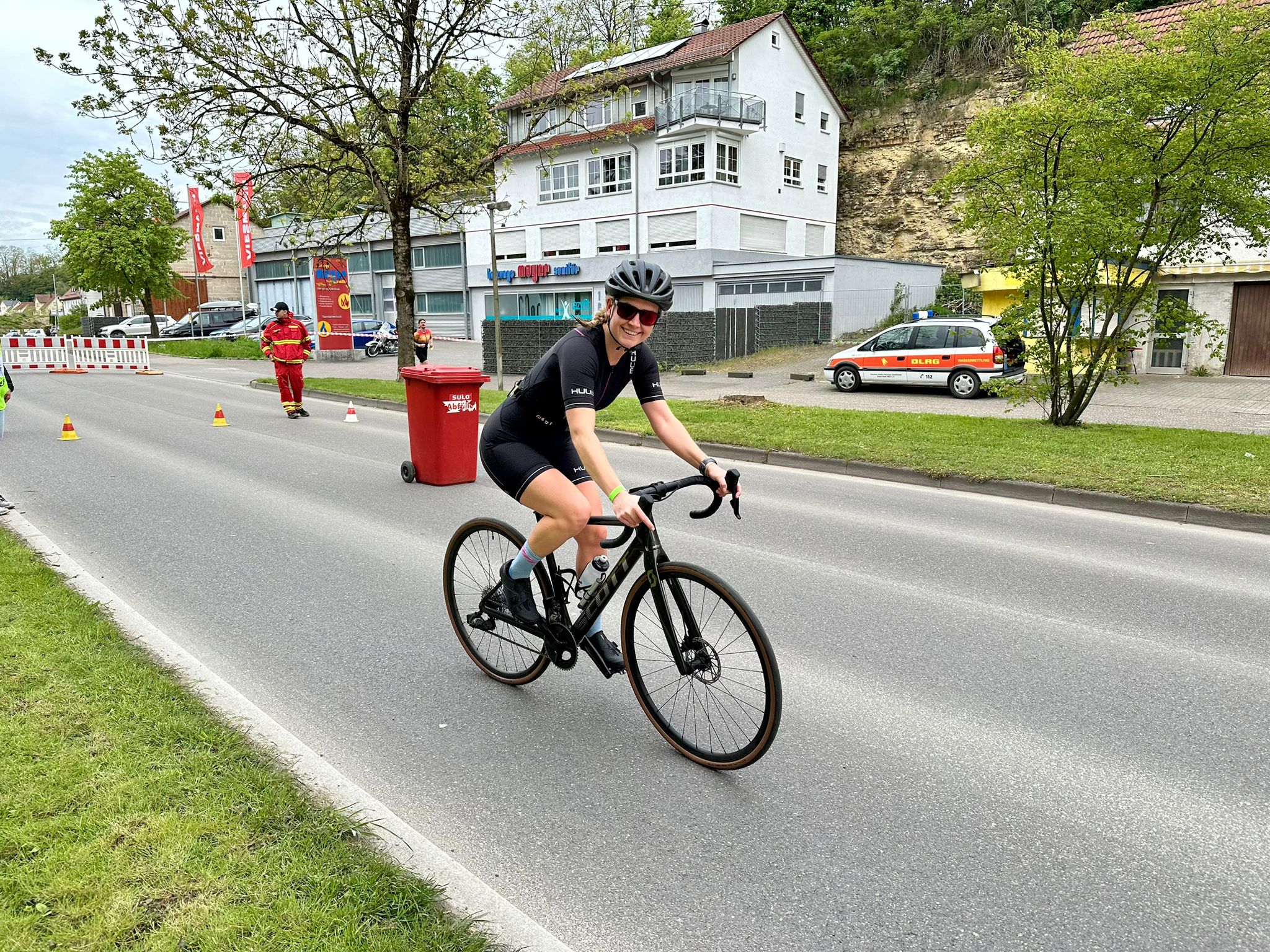 Eine junge Frau fährt auf einem Rennrad. Sie trägt einen schwarzen Einteiler und lacht ins Bild. 